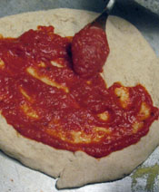 Spread tomato sauce on the raw dough, leaving an edge